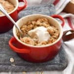 A mini cocotte full of freshly baked apple crisp and topping with a scoop of ice cream