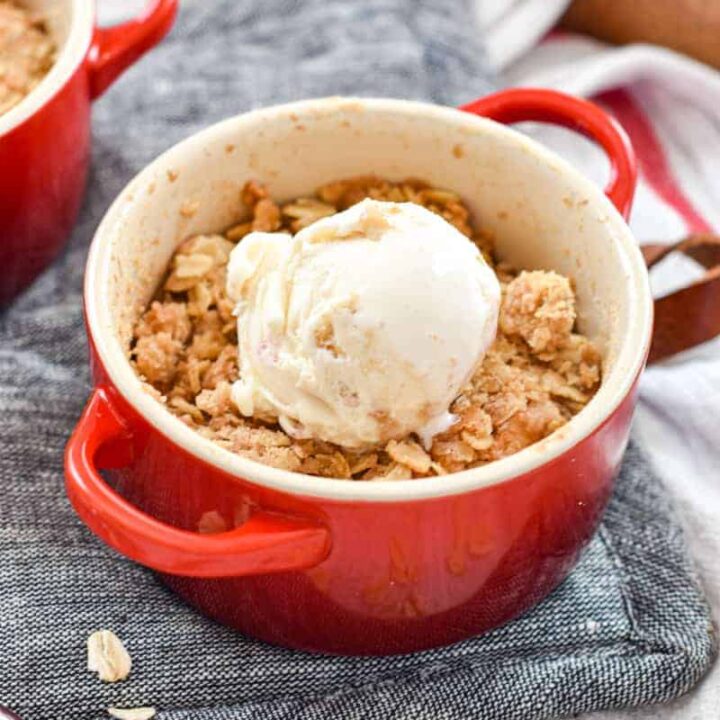 A mini cocotte full of freshly baked apple crisp and topping with a scoop of ice cream
