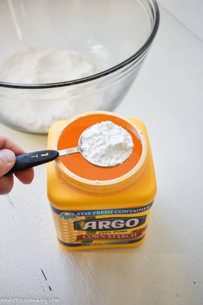 A tablespoon of cornstarch being scooped from a yellow container
