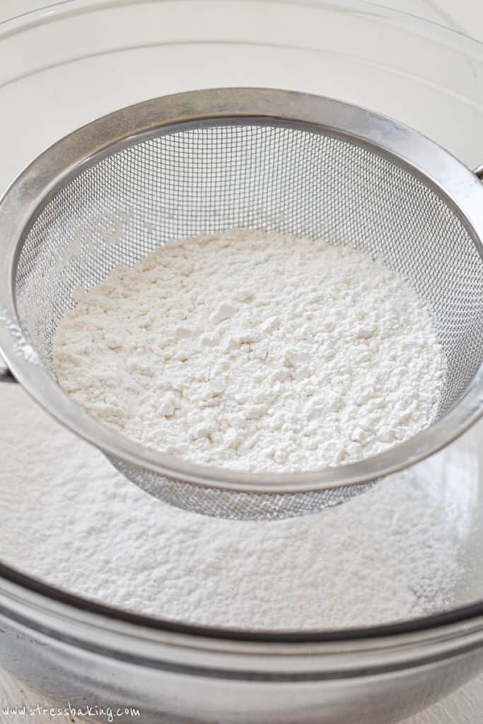 A mesh sieve full of cake flour over a glass bowl