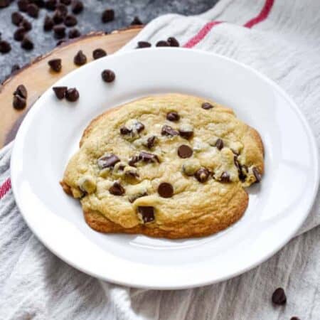 Giant crinkly chocolate chip cookie with a chunk missing on a white plate