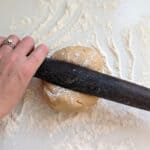 A round of cookie dough being rolled out on a floured surface