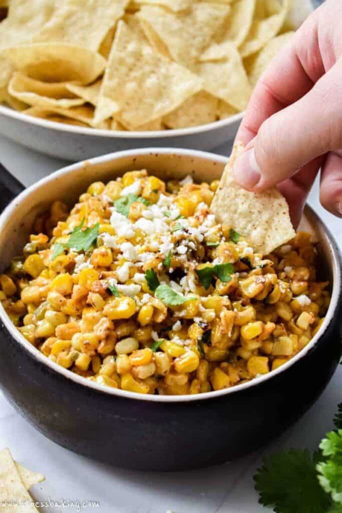 A chip being dipped into crock of Mexican corn dip