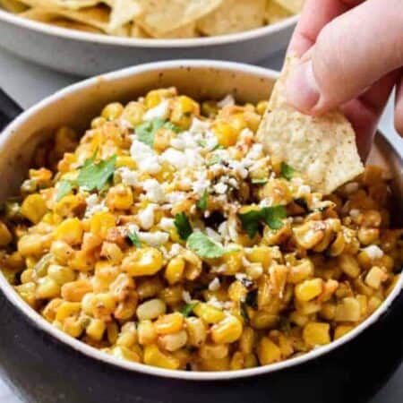 A chip being dipped into crock of Mexican corn dip