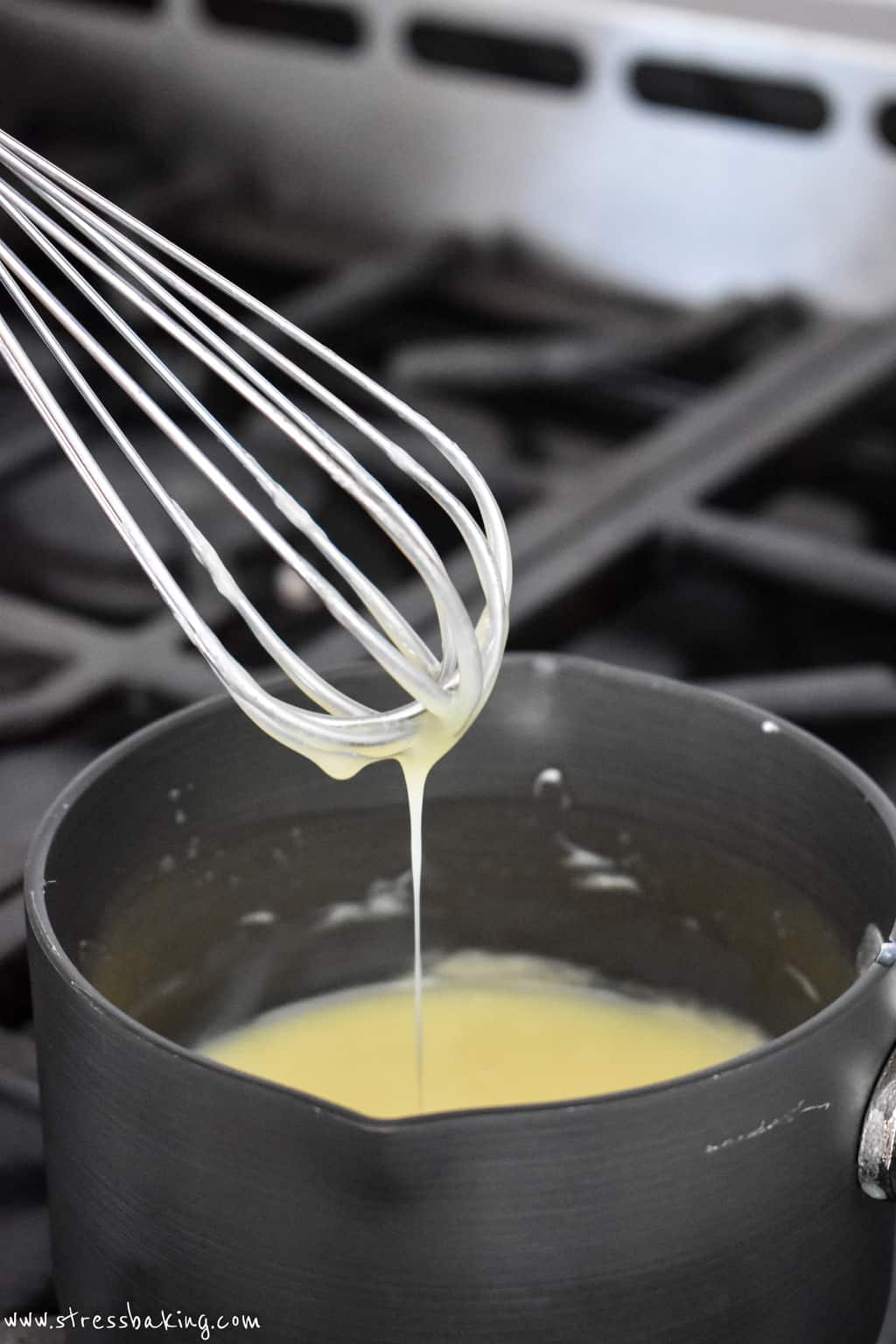 A whisk lifting white chocolate sauce out of a small saucepan