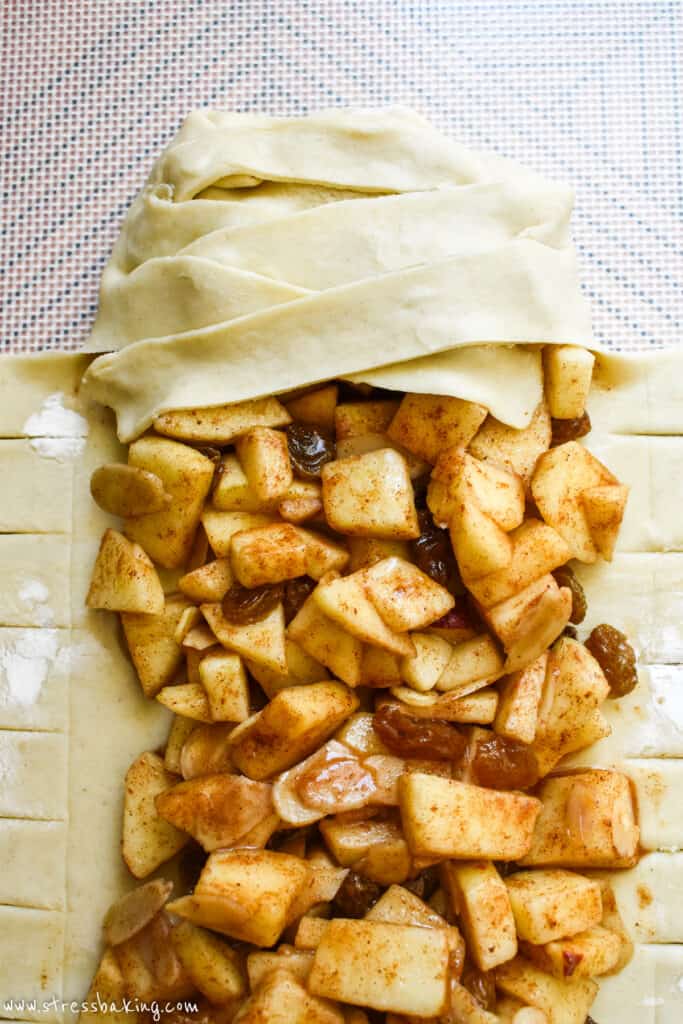 Puff pastry being braided over apple strudel filling