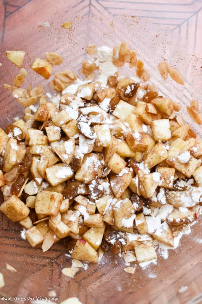 Diced apples and raisins coated in cinnamon sugar and flour in a clear bowl