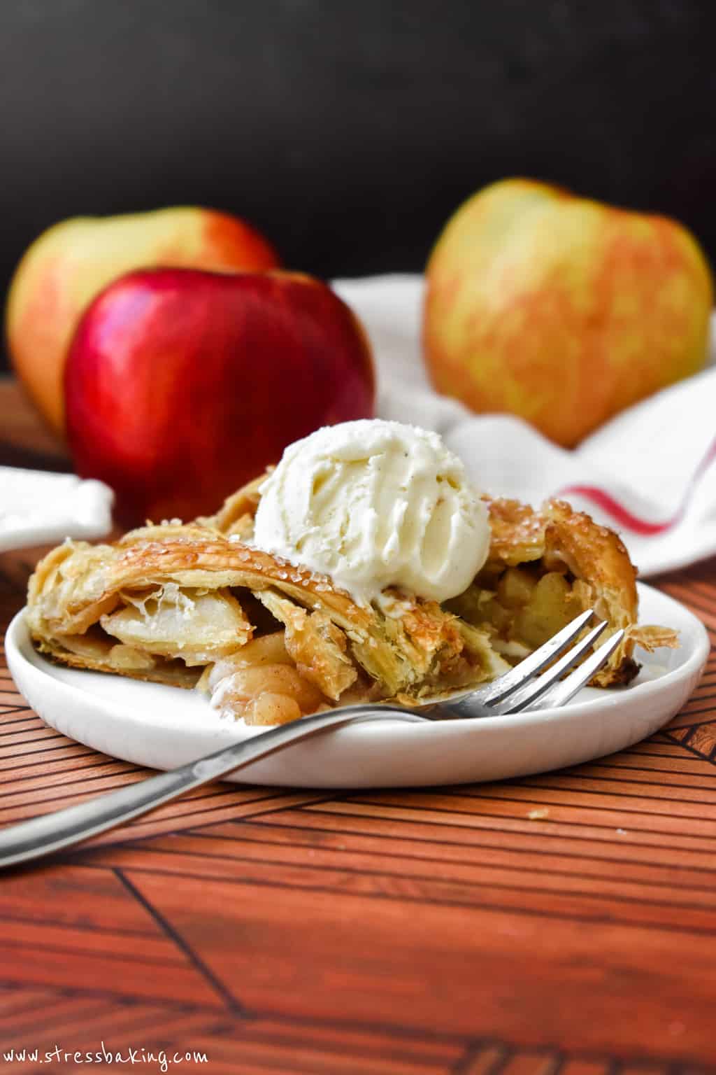 Slices of golden apple strudel on a small white plate with a scoop of vanilla ice cream on top