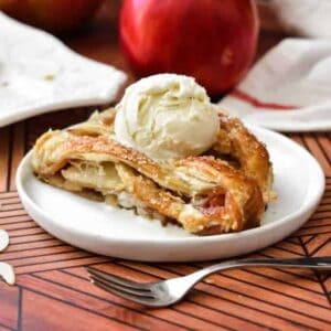 Slices of golden apple strudel on a small white plate with a scoop of vanilla ice cream on top