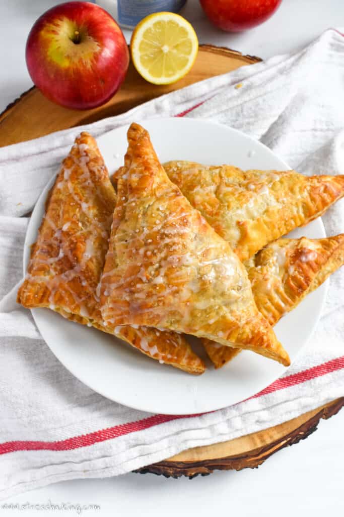 A pile of apple turnovers drizzled with glaze and sparkling sugar on a white plate
