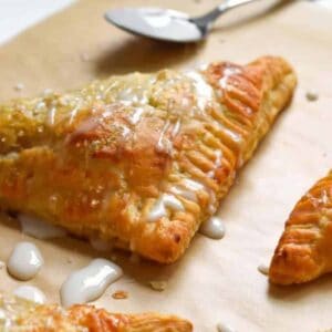Closeup of apple turnovers on parchment paper drizzled with icing