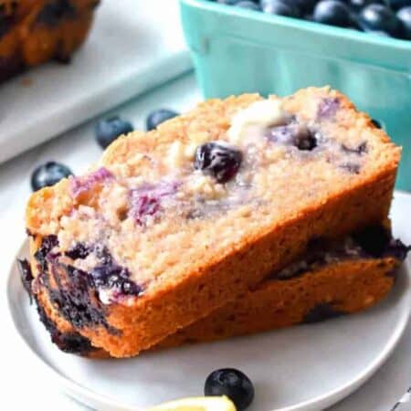 Two slices of blueberry muffin bread slathered with butter on a white plate
