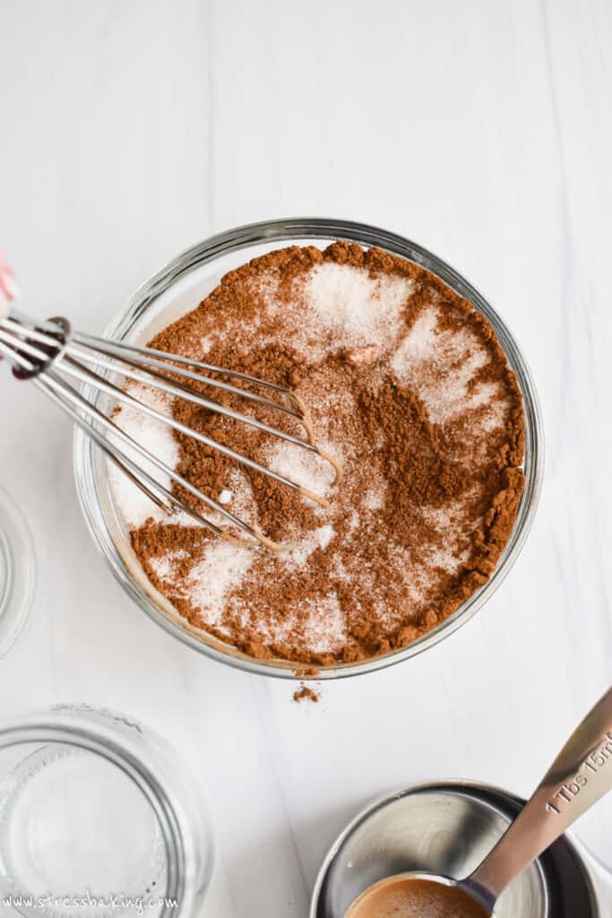 A glass bowl with cinnamon and sugar being whisked together on a white counter