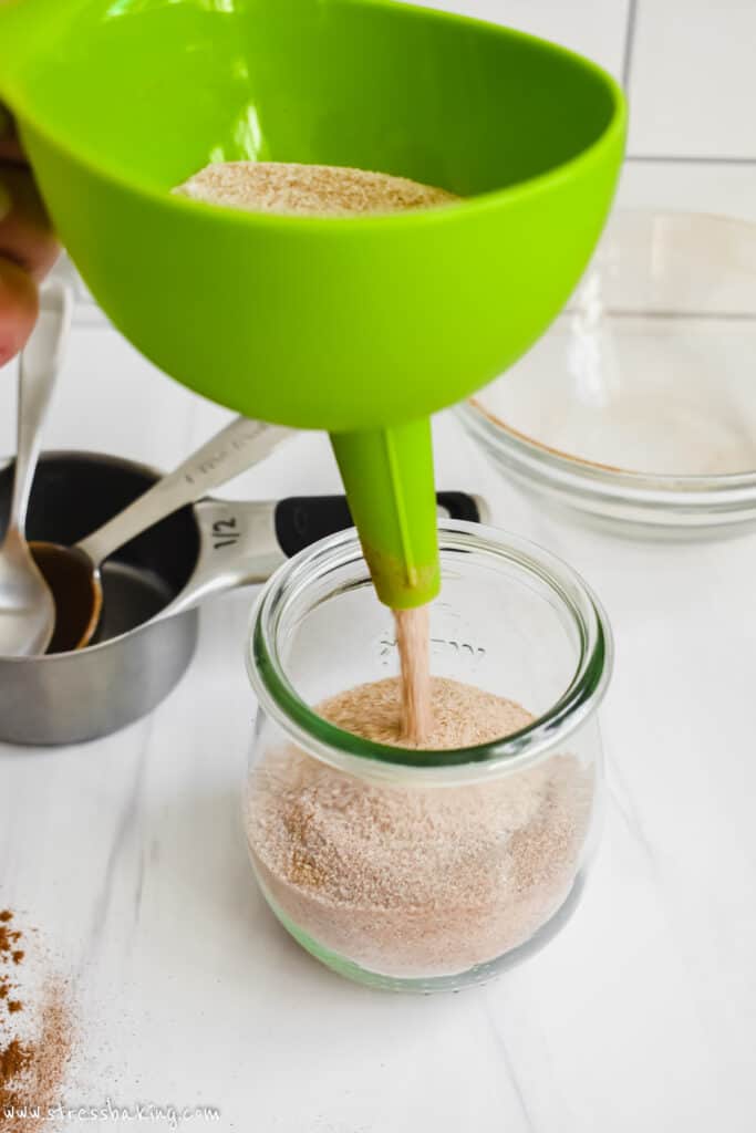 Cinnamon sugar being poured through a bright green funnel into a glass Weck jar