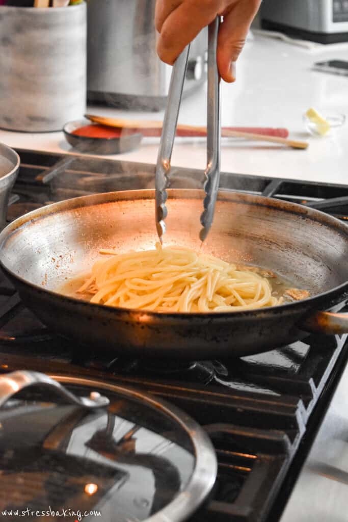 Spaghetti being added to a saute pan with tongs