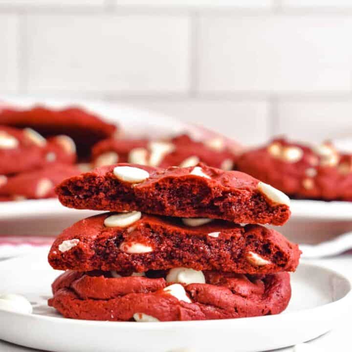 A stack of red velvet cookies on a white plate broken in half to show the sift middles