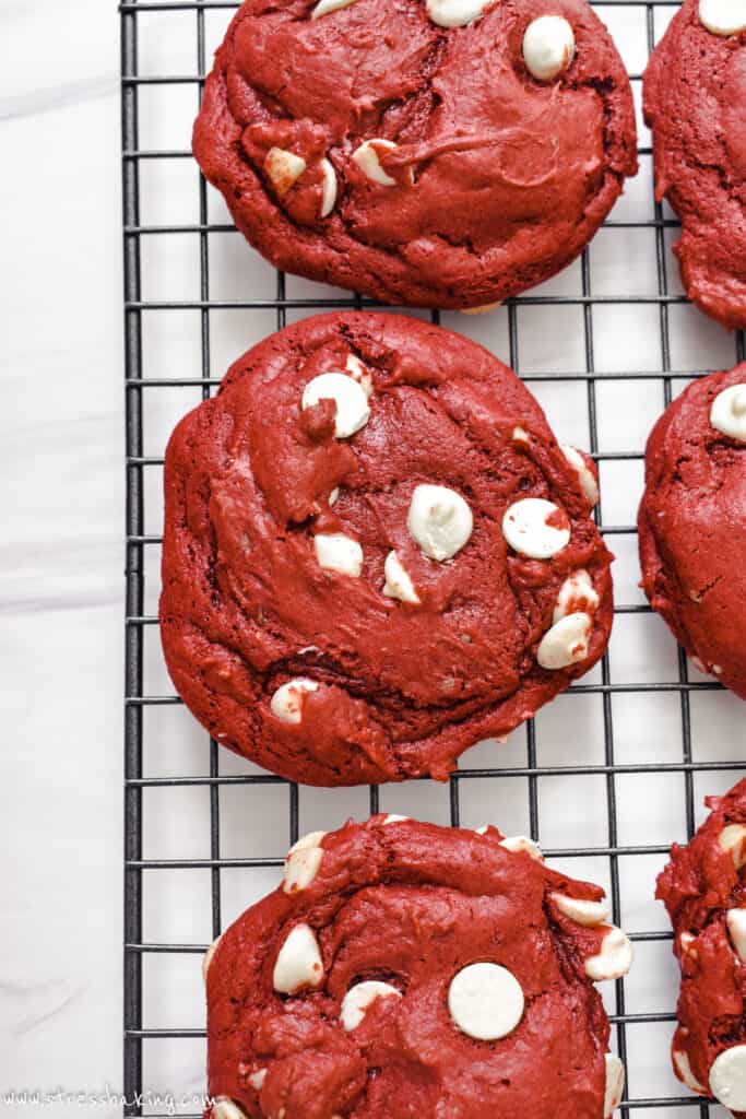 Red velvet cookies with white chocolate chips cooking on a black wire rack