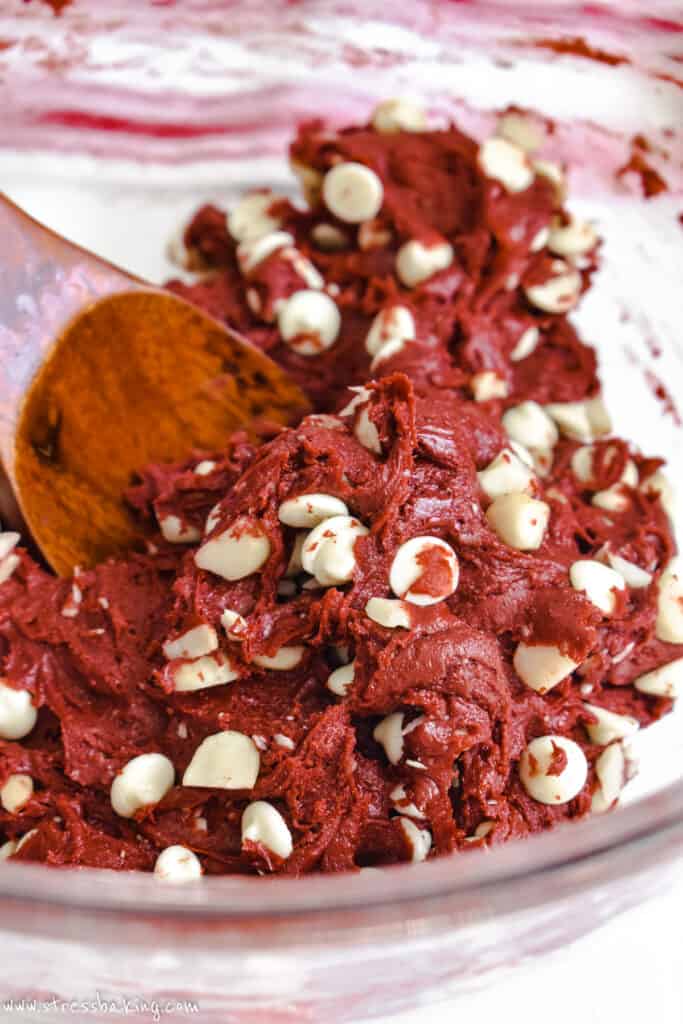 Bright red cake mix dotted with white chocolate chips in a clear mixing bowl