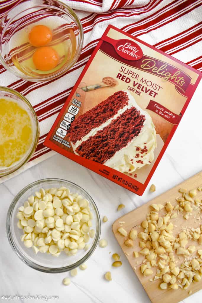 A box of red velvet cake mix, white chocolate chips, nuts, eggs and melted butter on a counter