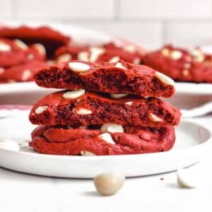 A stack of red velvet cookies on a white plate broken in half to show the soft middles