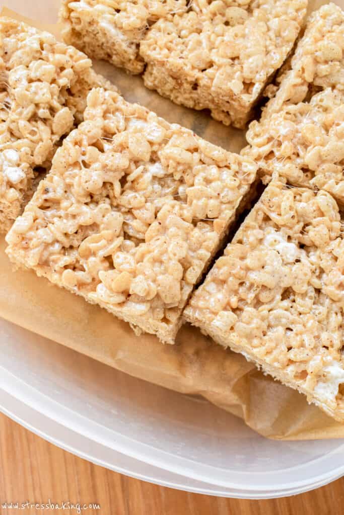 Rice krispie treats stacked on parchment paper in a tupperware container