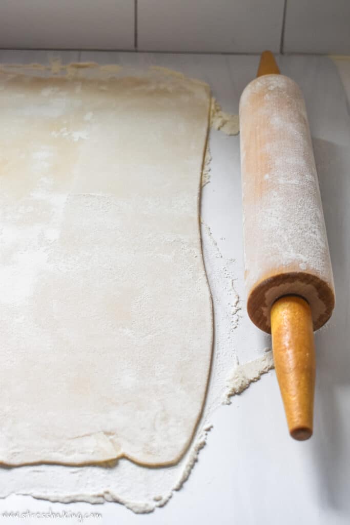 A pie crust unrolled on a white floured countertop next to a rolling pin