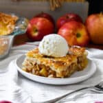 A huge slice of apple pie with a golden brown crust and topped with vanilla ice cream