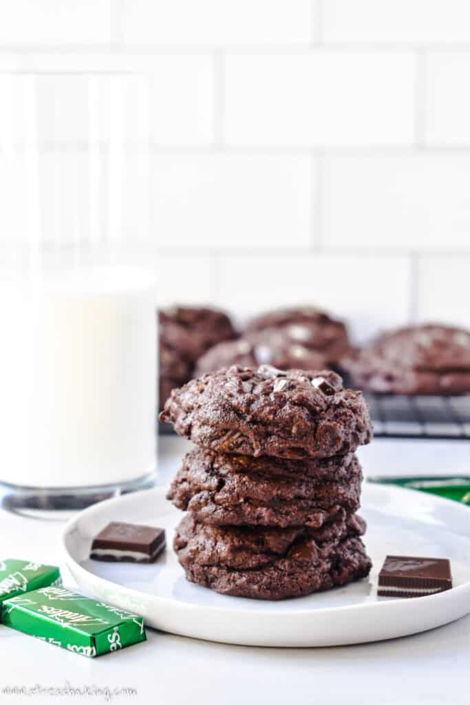 A stack of chocolate cookies with Andes mints next to a glass of milk