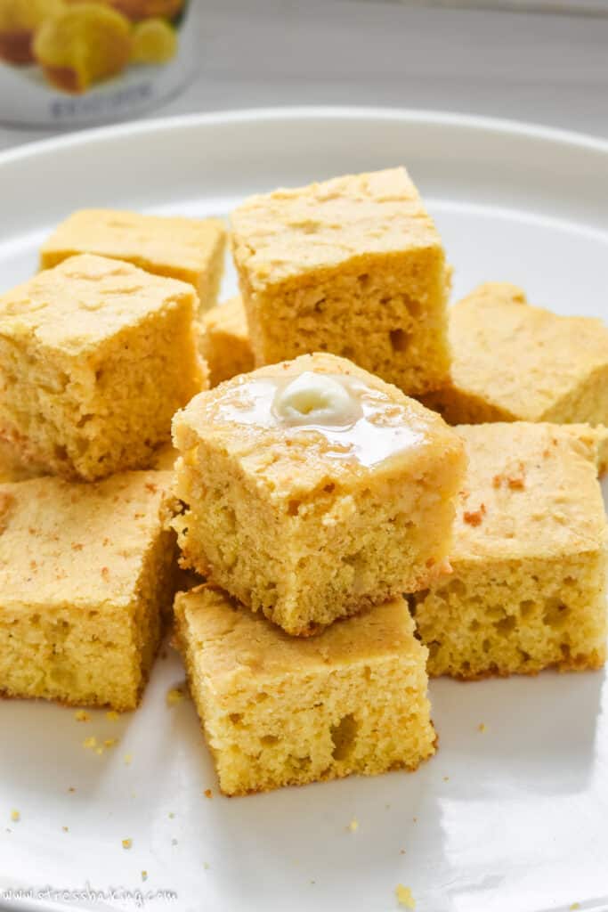 Squares of cornbread stacked on a white platter topped with melting butter