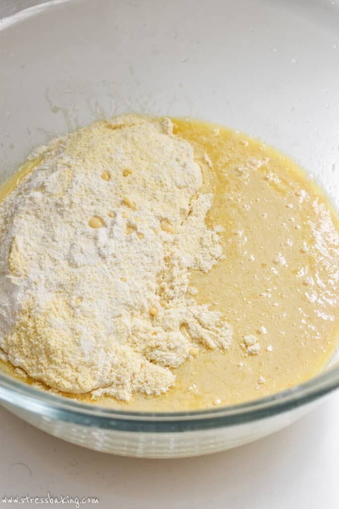 A clear bowl full of yellow wet and dry ingredients before being combined