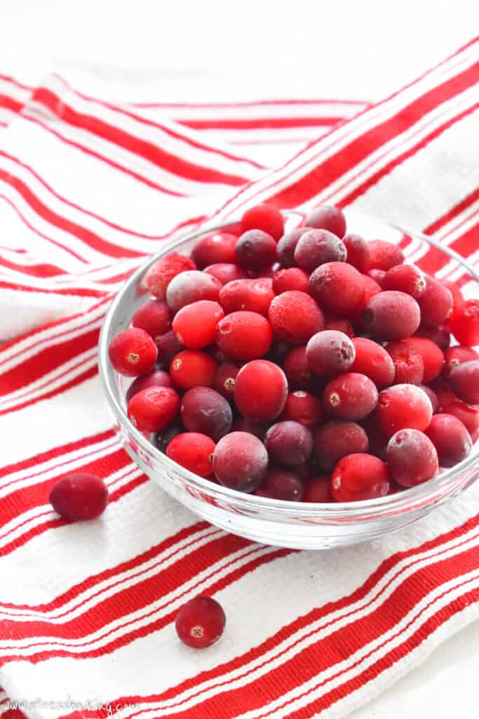 Small clear bowl of frozen cranberries on a white and red stripped dishtowel