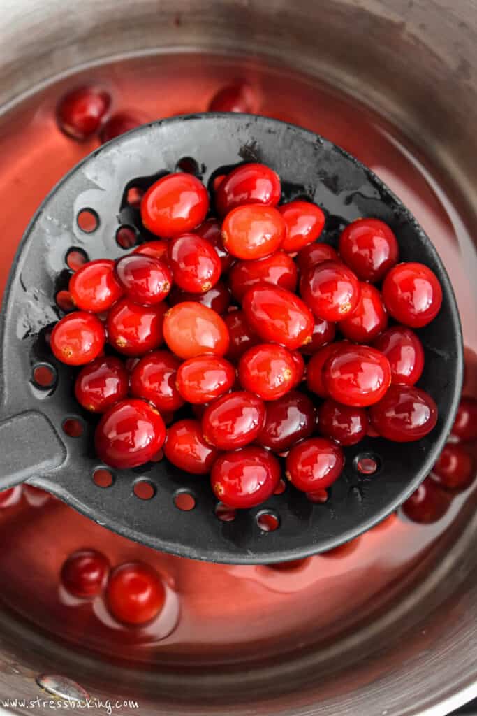 Bright red cranberries in a slotted spoon above a saucepan