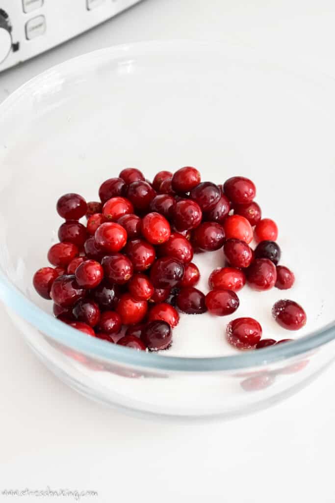 Bright red cranberries in a clear bowl of white sugar