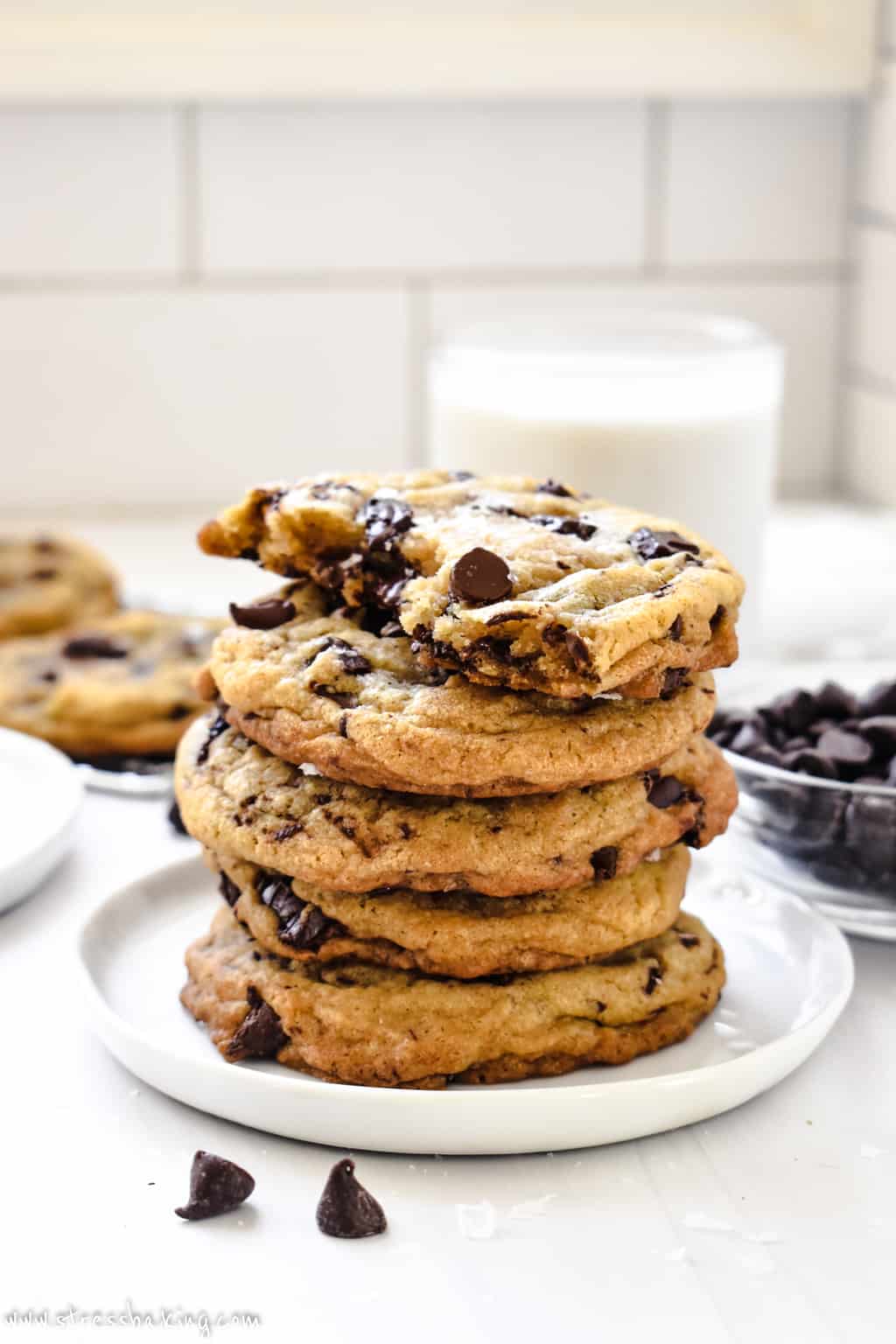 A stack of chocolate chip cookies on a small white plate in front of a glass of milk