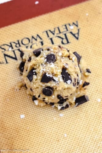 Chocolate chip cookie dough ball sprinkled with flaky salt on a baking sheet