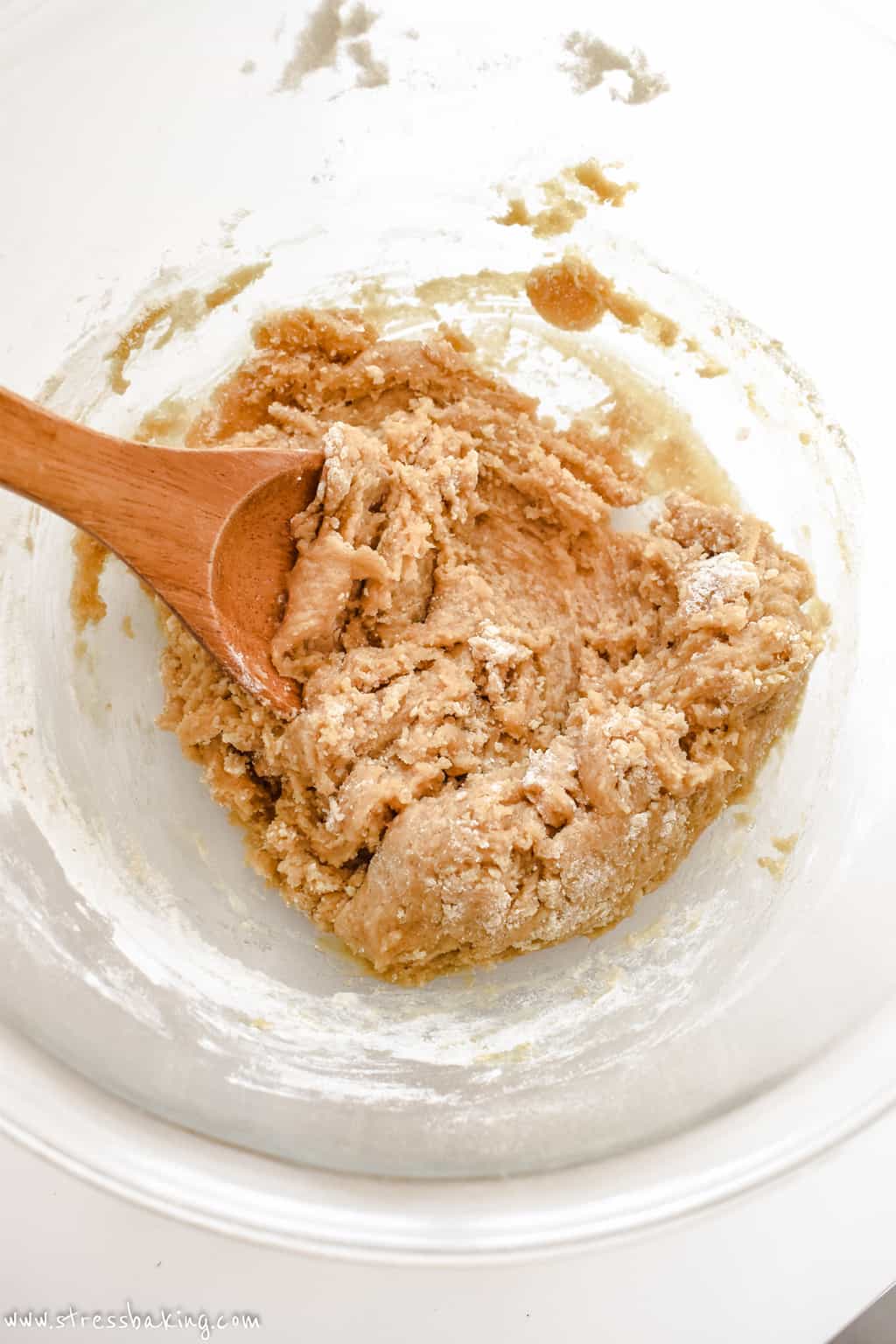 Tan cookie dough being mixed with a wooden spoon in a clear bowl