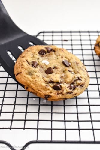 A chocolate chip cookie being placed on a wire rack with a black spatula
