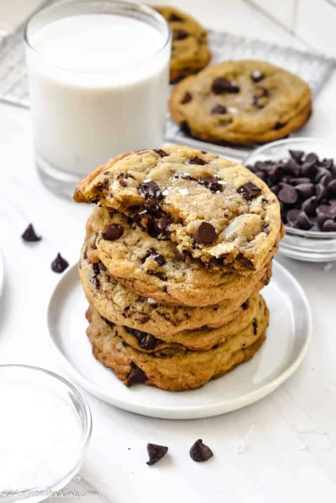 A stack of chocolate chip cookies on a small white plate in front of a glass of milk