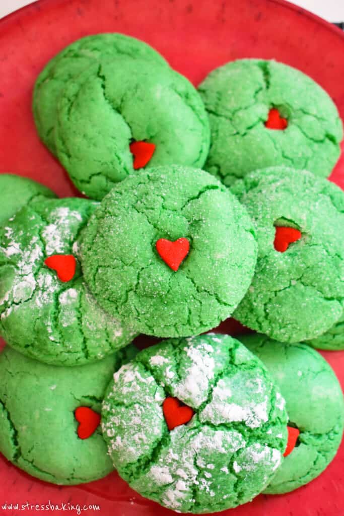 Bright green crinkly cookies stacked on a red plate with red heart sprinkles on top