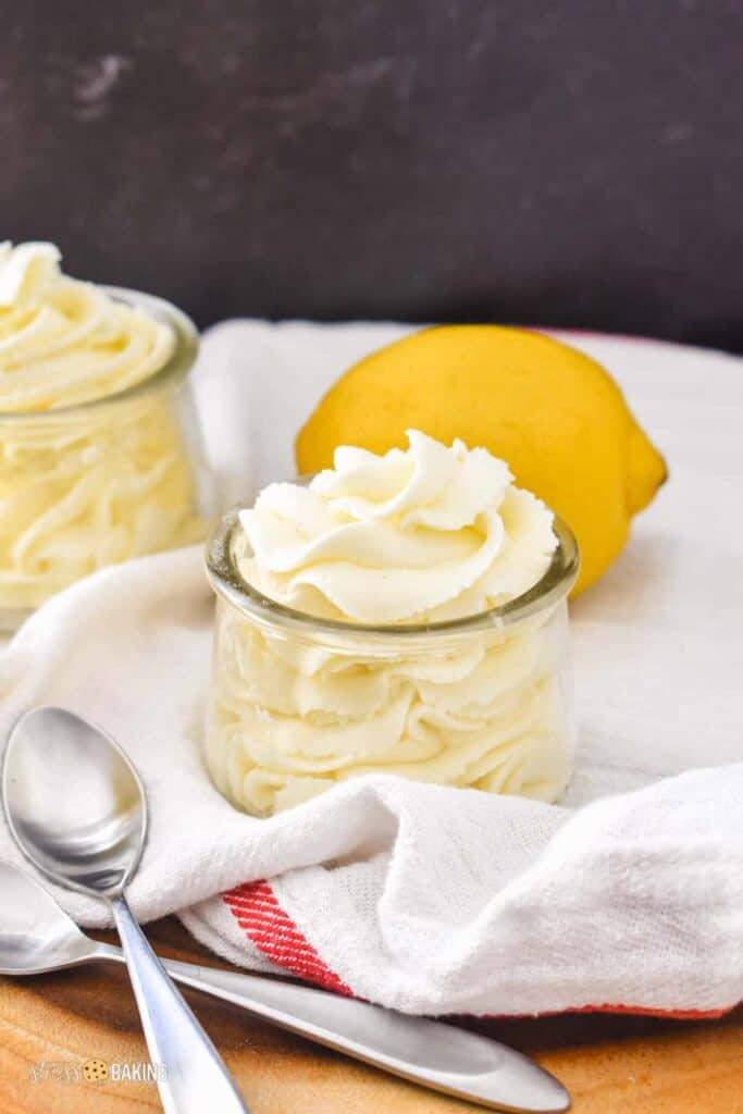 A small glass jar of light yellow mousse with spoons and lemons in the background