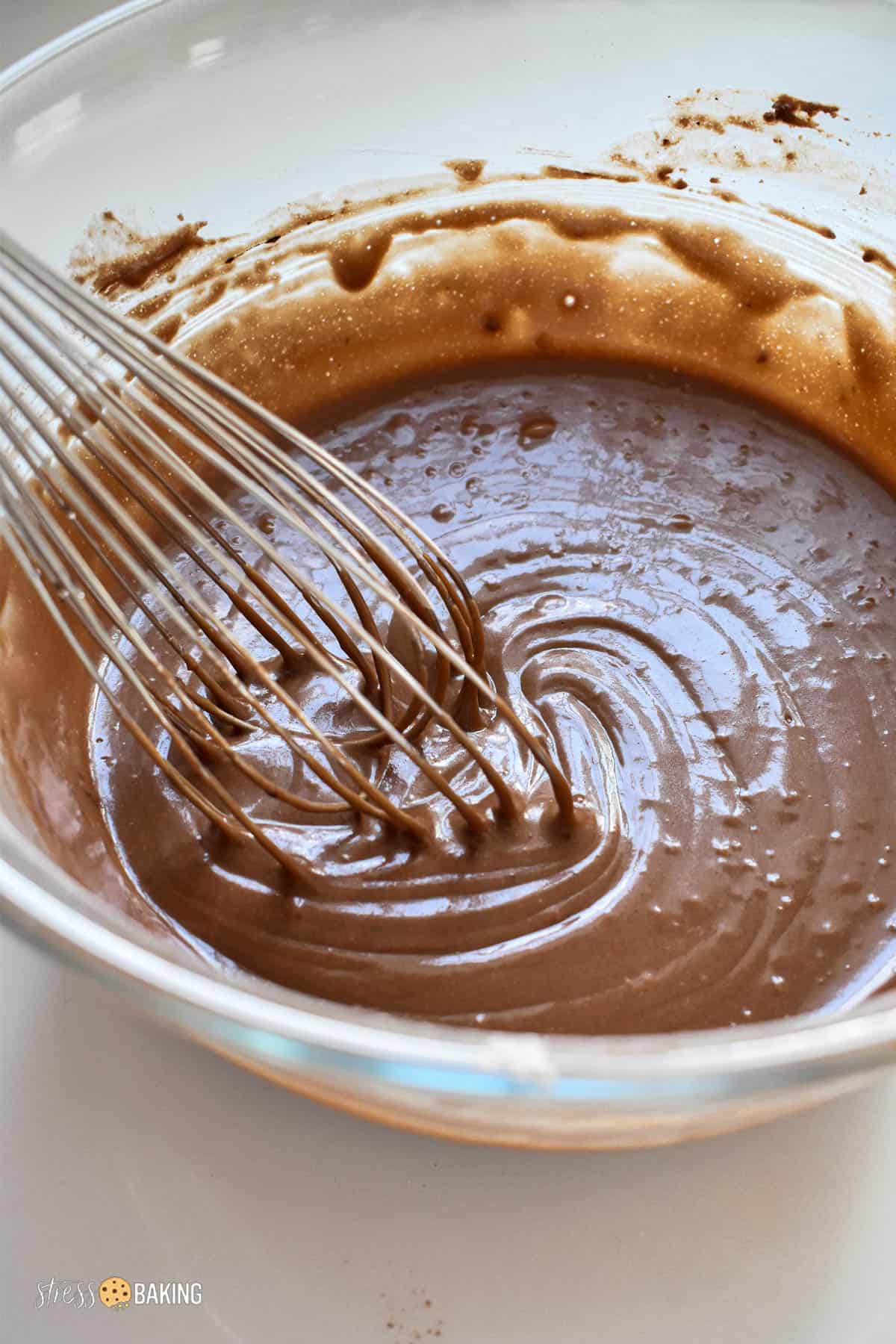 Creamy chocolate cake batter in a clear bowl with a whisk
