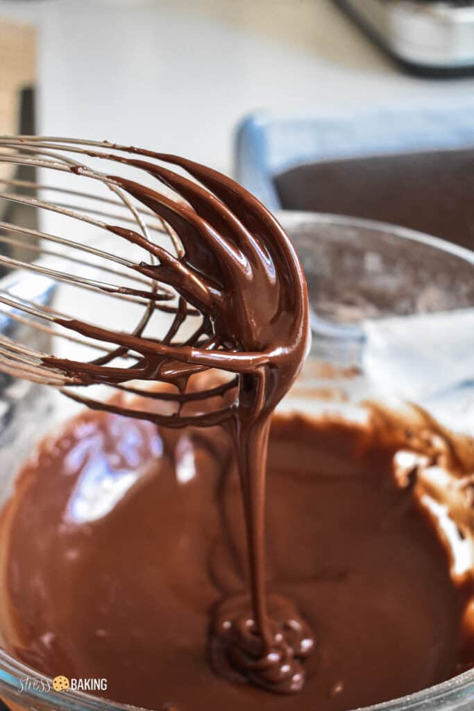 Smooth chocolate cake batter dripping off a whisk into a clear bowl