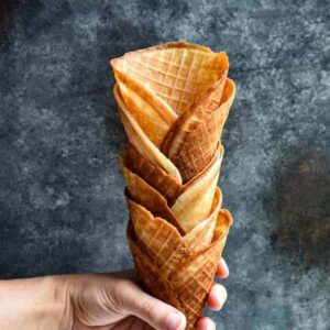 A hand holding a stack of homemade golden waffle cones