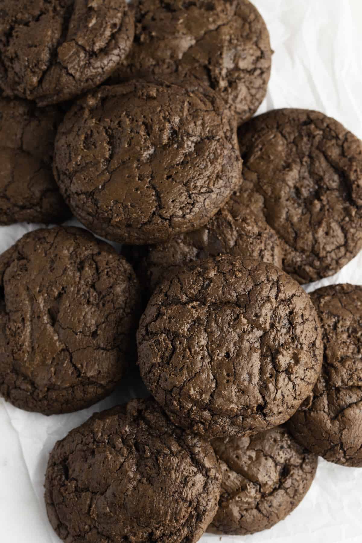 Pile of crinkly brownie cookies on a white surface