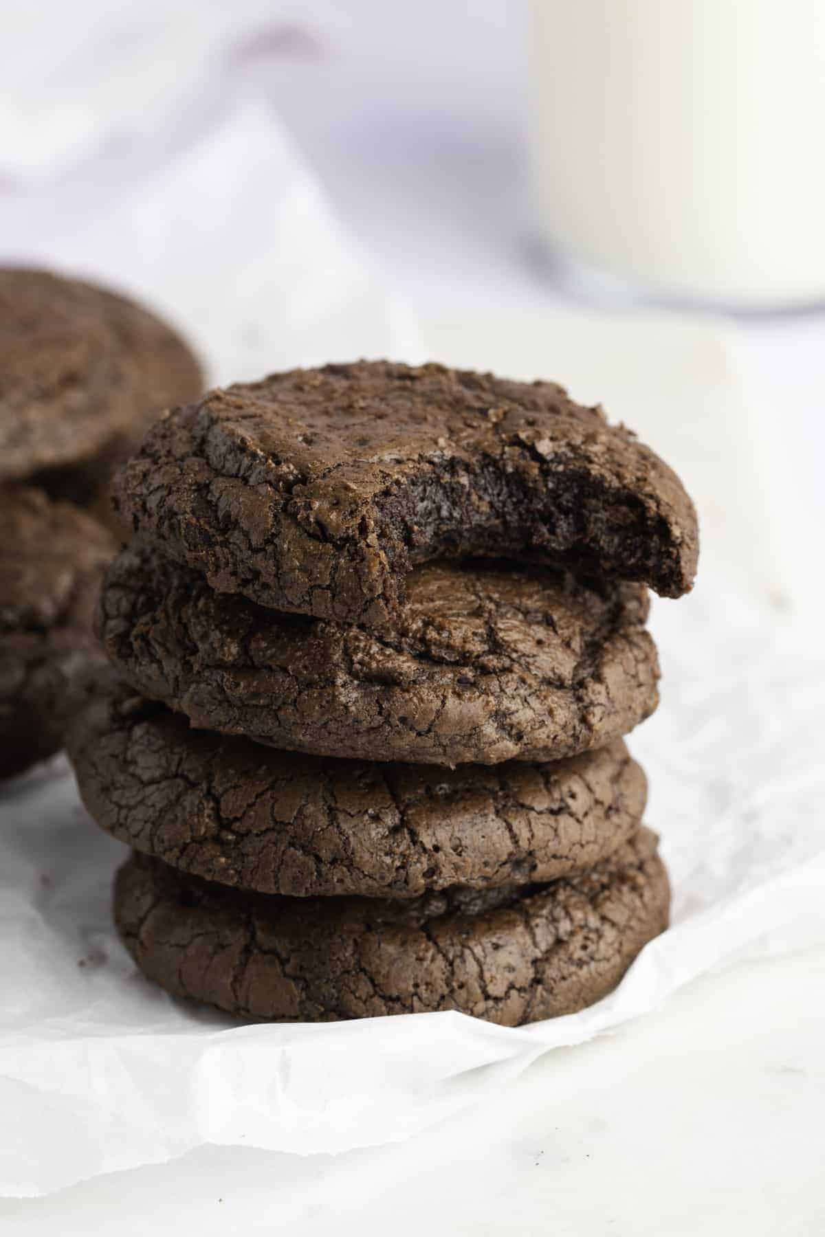 Stack of crinkly brownie cookies with a bite taken out to show the fudgy center