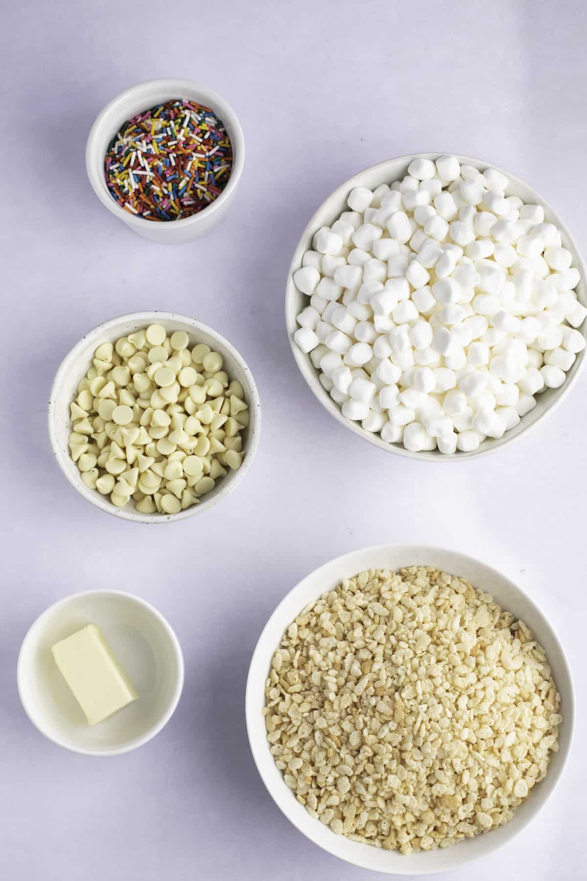 Ingredients for funfetti rice krispie treats in small bowls on a white surface