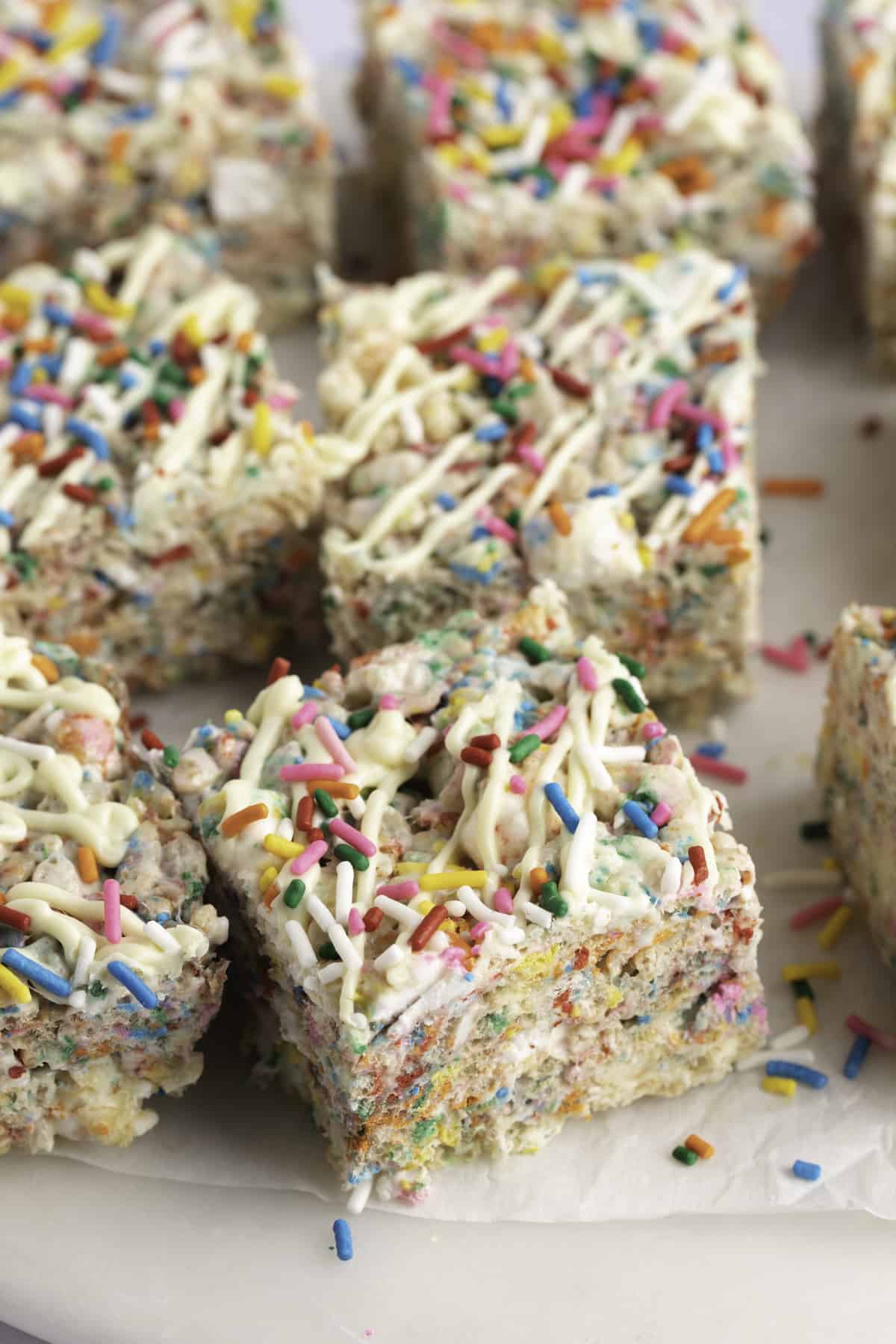 Squares of brightly colored funfetti rice krispie treats drizzle with white chocolate and sprinkles