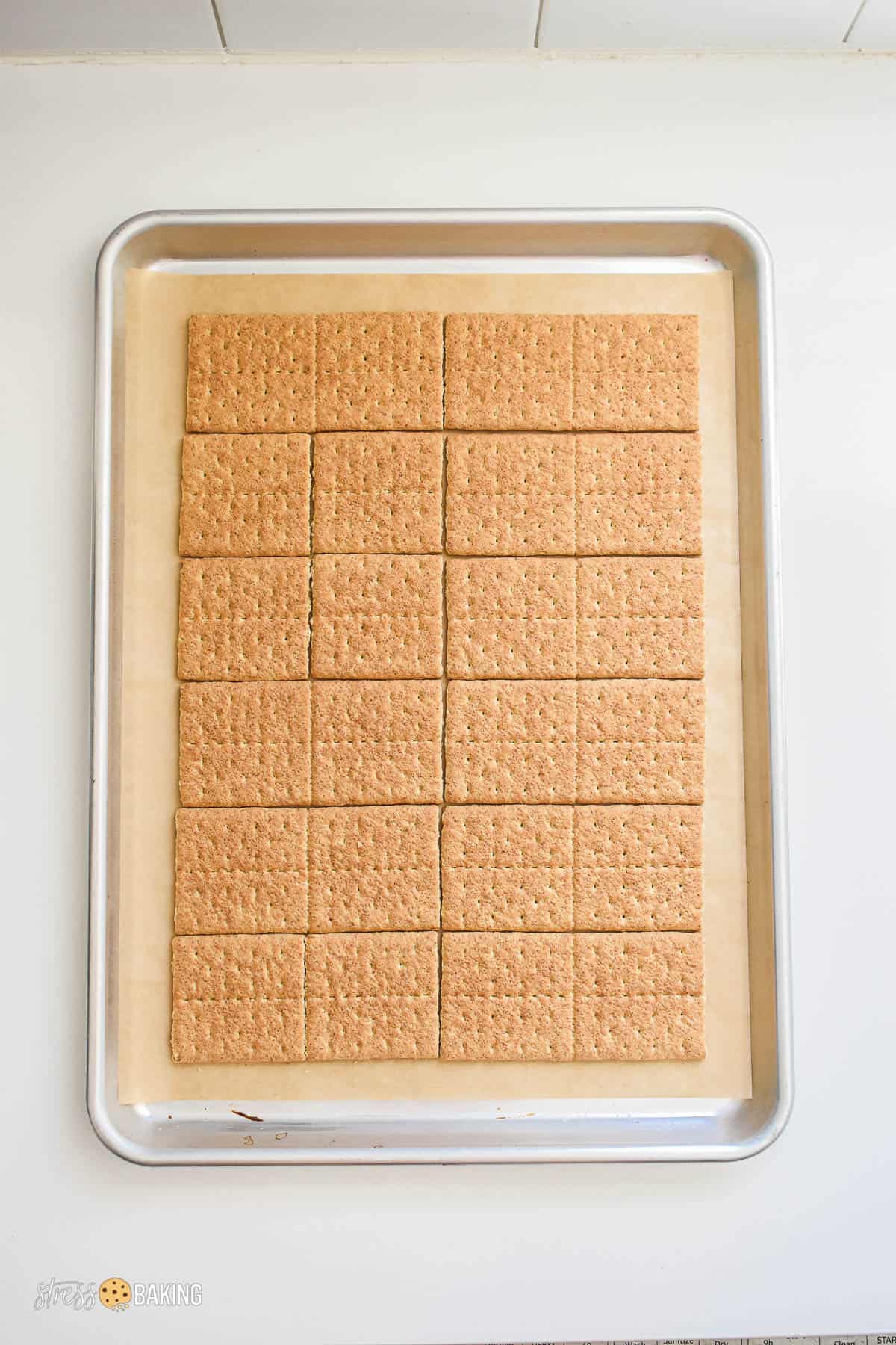 Graham crackers lined up on an aluminum pan lined with parchment paper