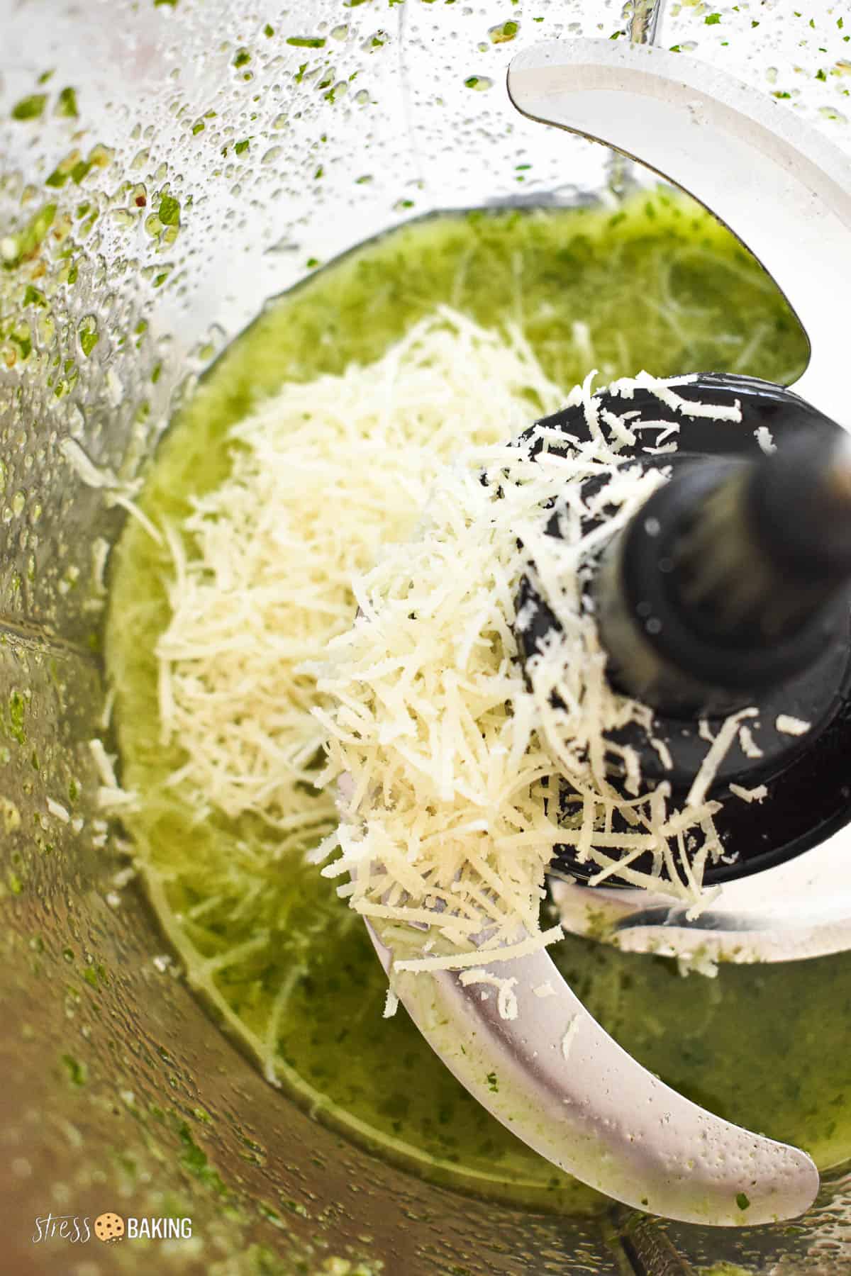 Shredded parmesan cheese being added to pesto in a food processor