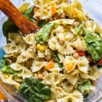Vibrant and colorful pesto pasta salad with spinach in a clear bowl with wooden serving spoons
